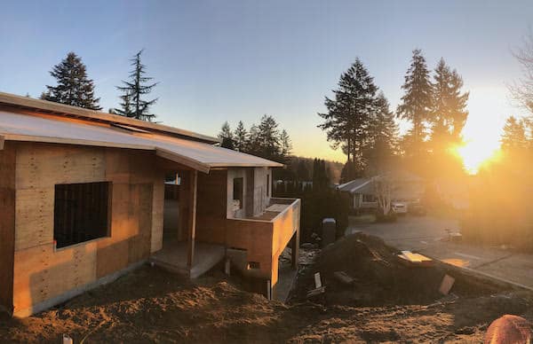 Under-construction house by White Wolf Homes with sunset and trees in background.