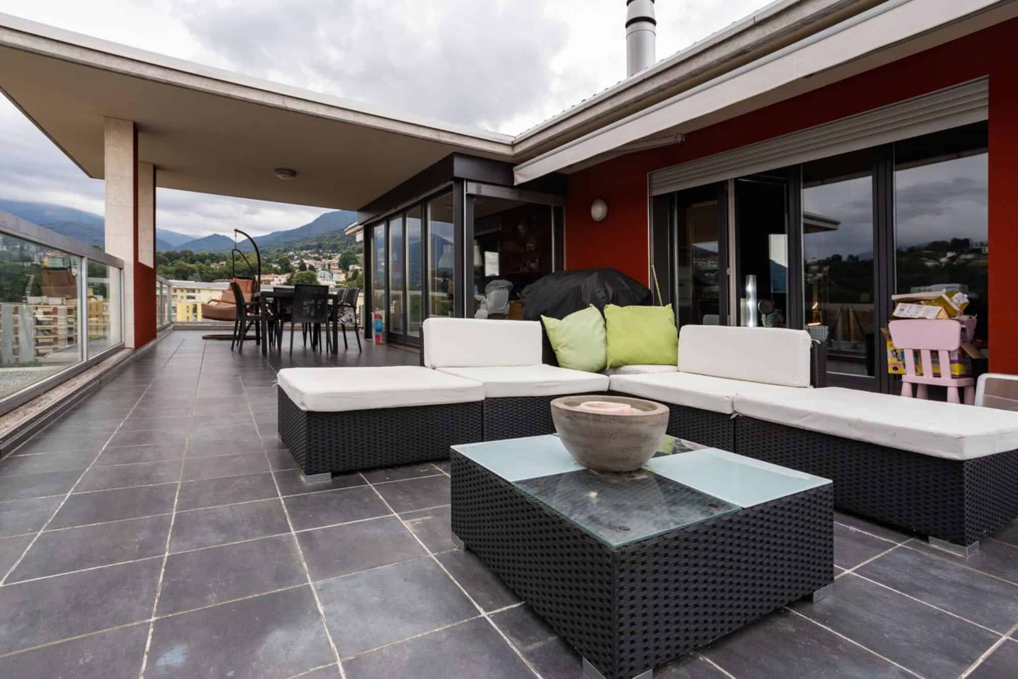 Modern outdoor living room on a terrace with sectional wicker seating and a glass-top fire table.