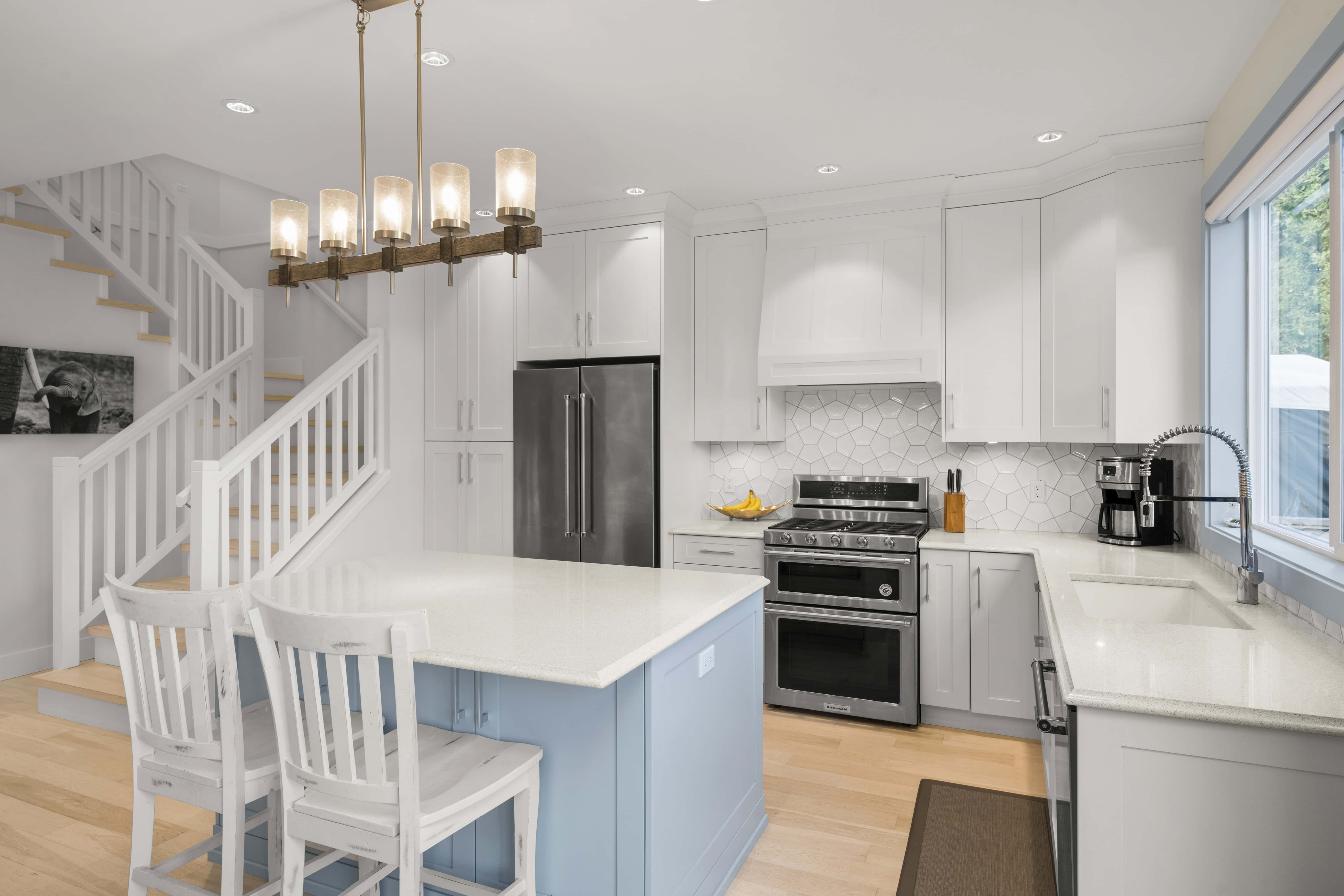 Modern white kitchen with island, stainless steel appliances and light blue island base.
