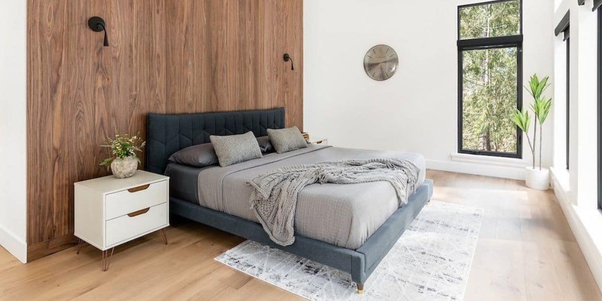 Modern master bedroom with wood accent wall, cozy bed, and natural light in Victoria BC.