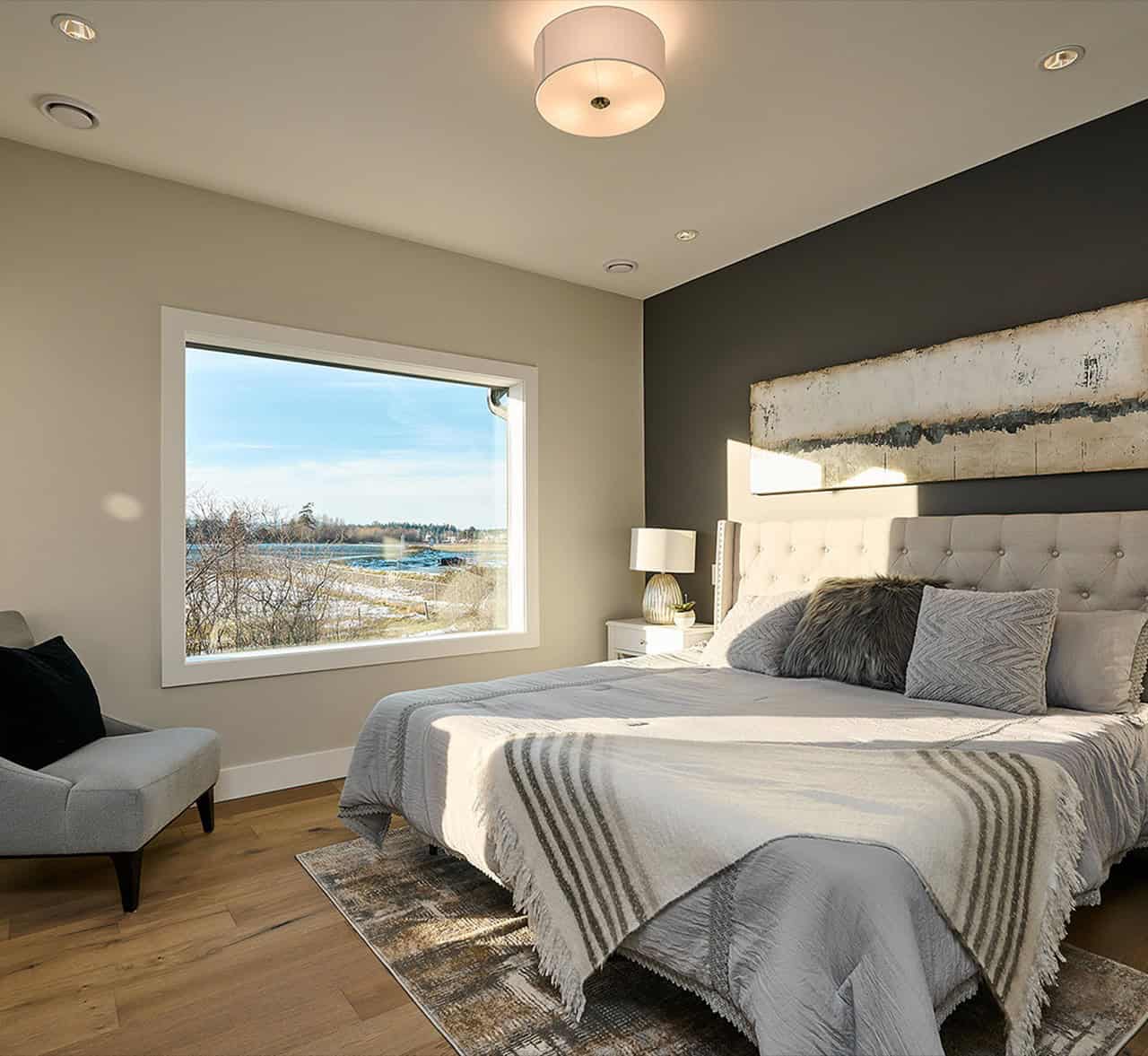 Bright bedroom with large window view of water and trees, king bed, neutral decor, and soft lighting.