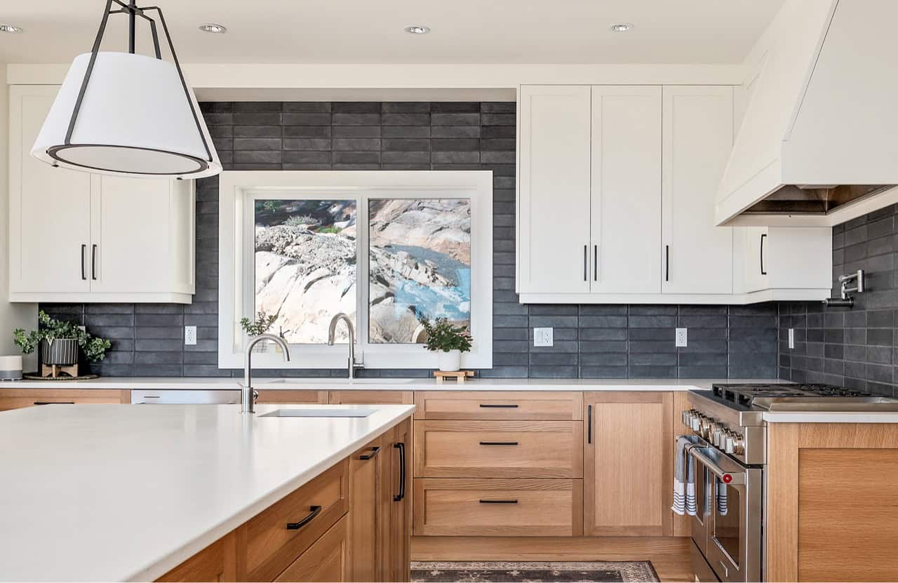 Bright kitchen with white upper cabinets, wood lower cabinets, and a large window over the sink.