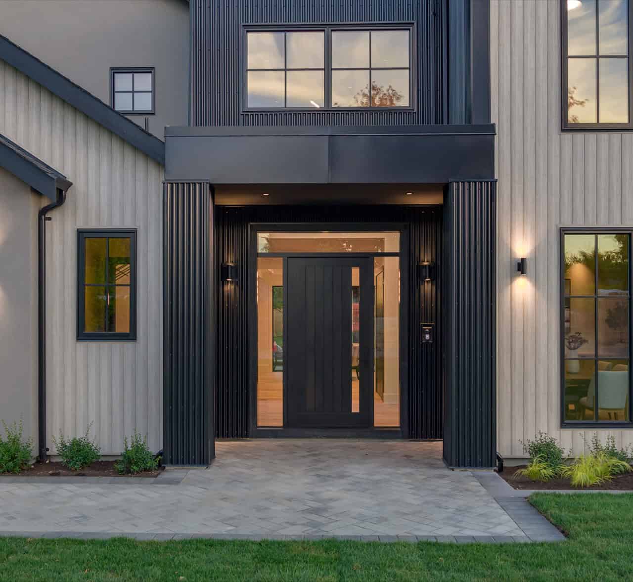 Modern two-story home entry with black accented columns and large glass doors.