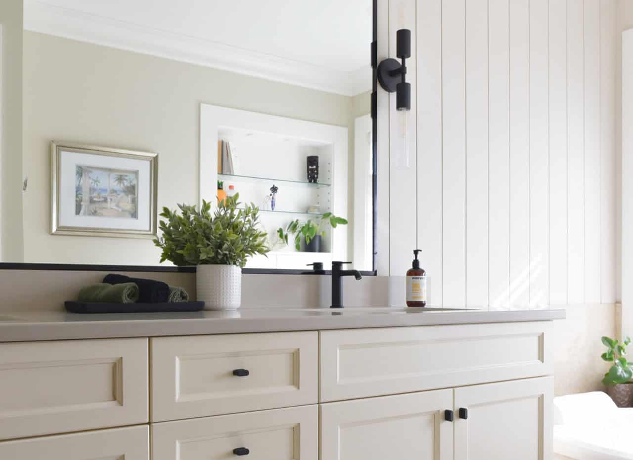 Bright bathroom vanity with white cabinetry, black faucet, and potted plant.