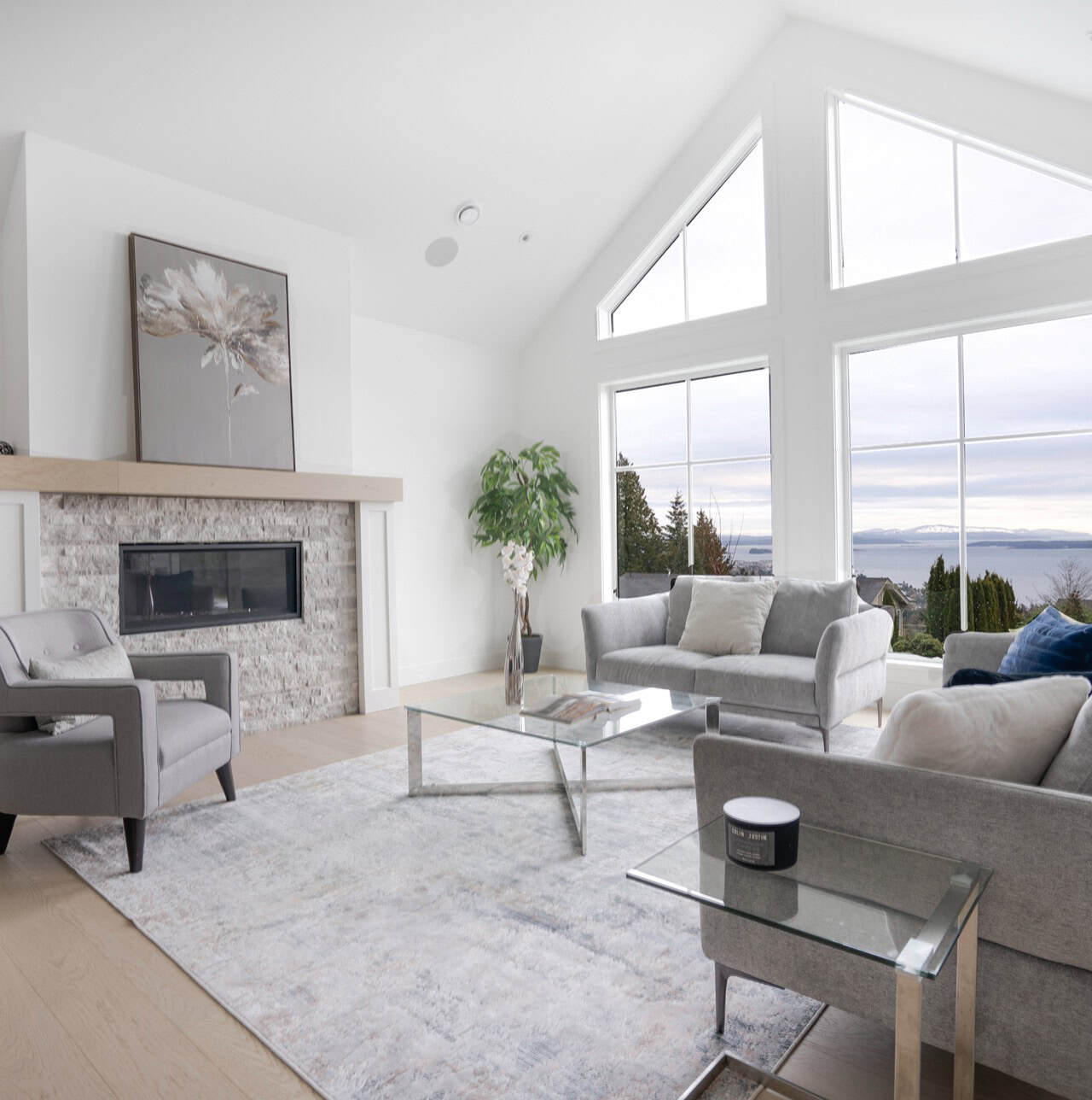 Bright living room with large windows, modern grey sofas, glass coffee table, and fireplace.