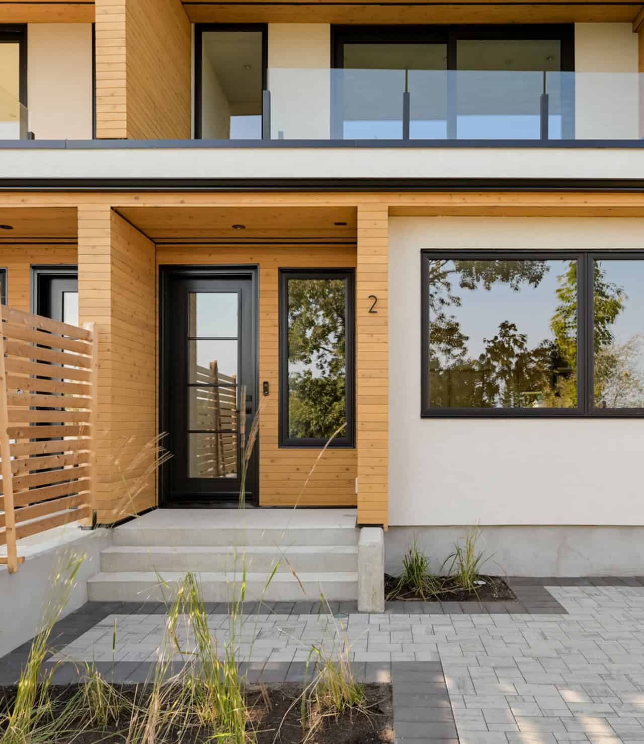 Modern two-story home entrance with wooden siding, black door, and large windows in a Victoria BC–in.