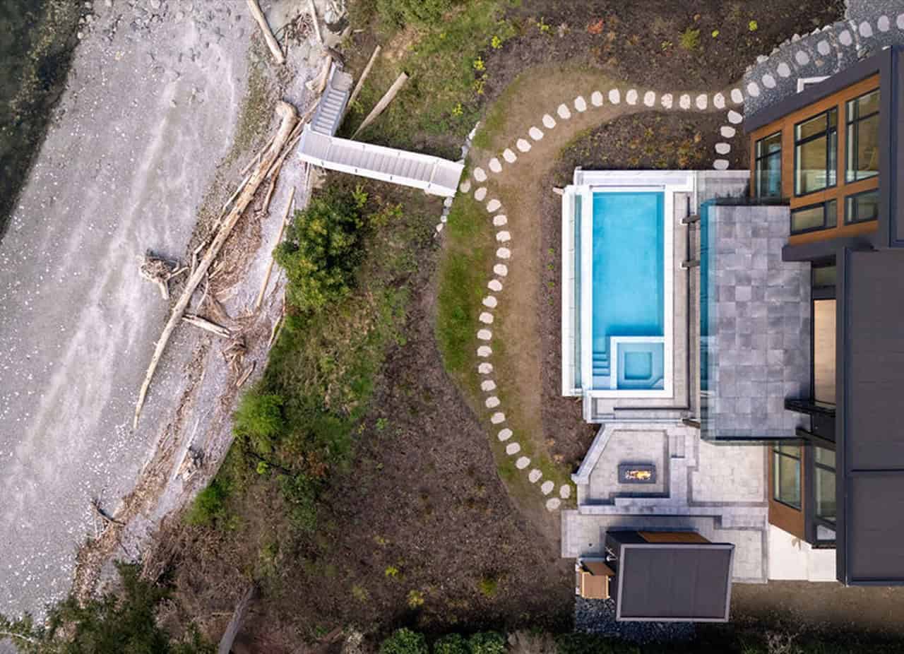 Aerial view of a modern villa by White Wolf Homes with a blue pool and stepping-stone path in a lush.