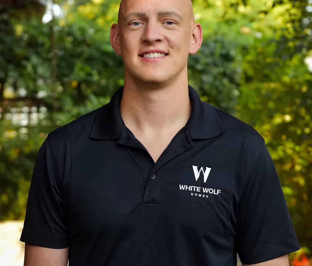 Team member wearing black polo with White Wolf Homes logo in outdoor setting.
