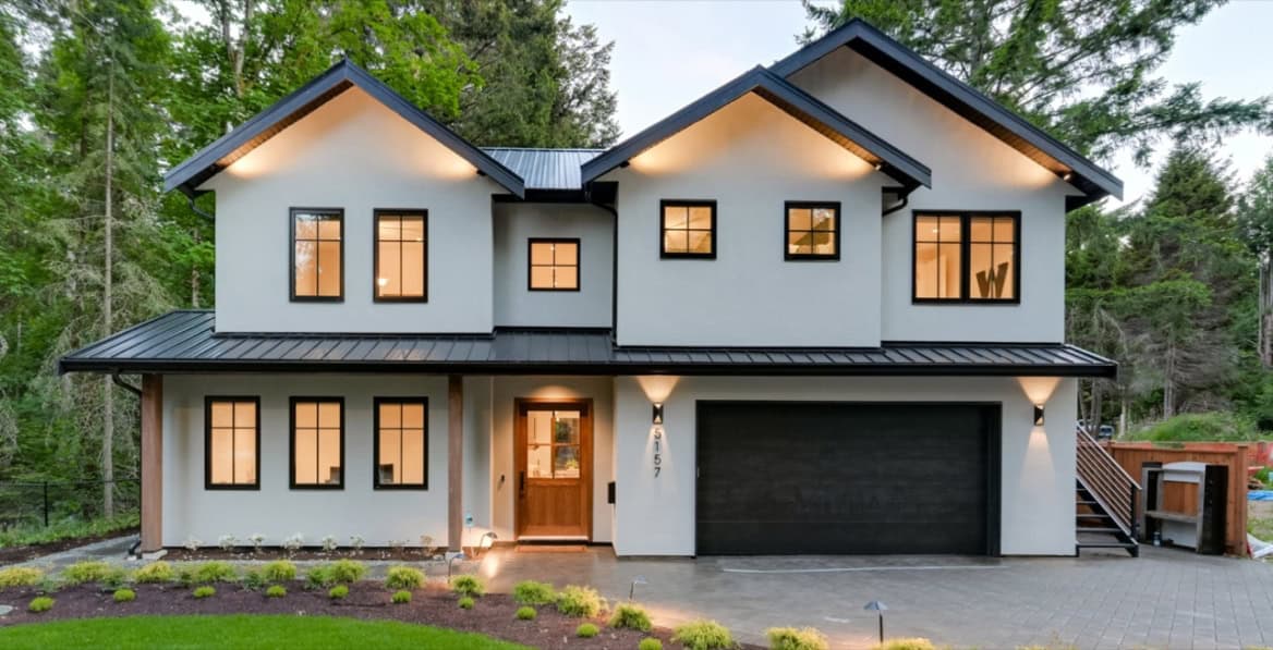 Modern two-story custom home with white exterior and black roof in a wooded setting.