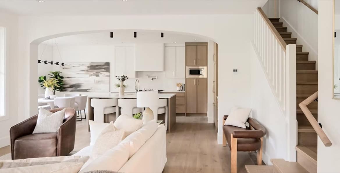 Bright, open-concept living area with white kitchen and staircase in a modern home.
