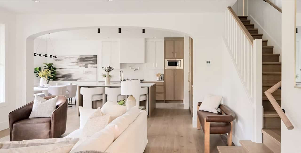 Bright, open-concept living area with white kitchen and staircase in a modern home.