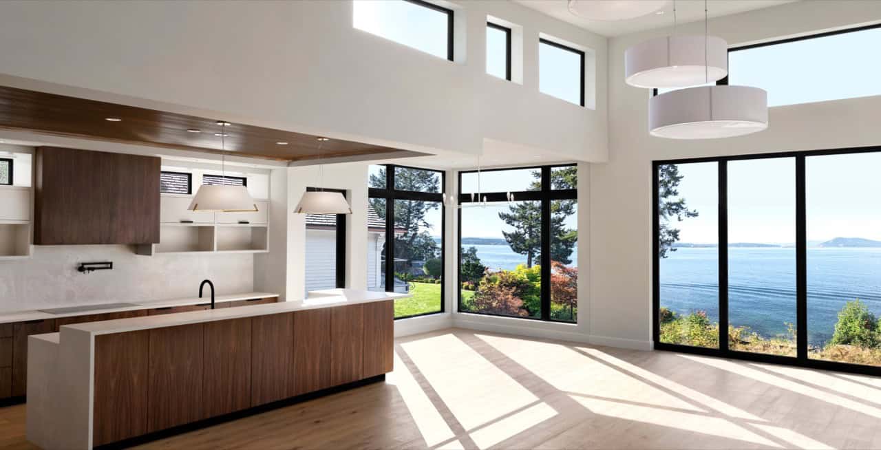 Open-concept kitchen with large windows overlooking water and coast, modern white and wood interior.