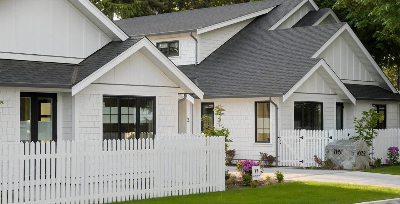 Victoria BC custom home exterior with white siding, grey roof, and white picket fence.