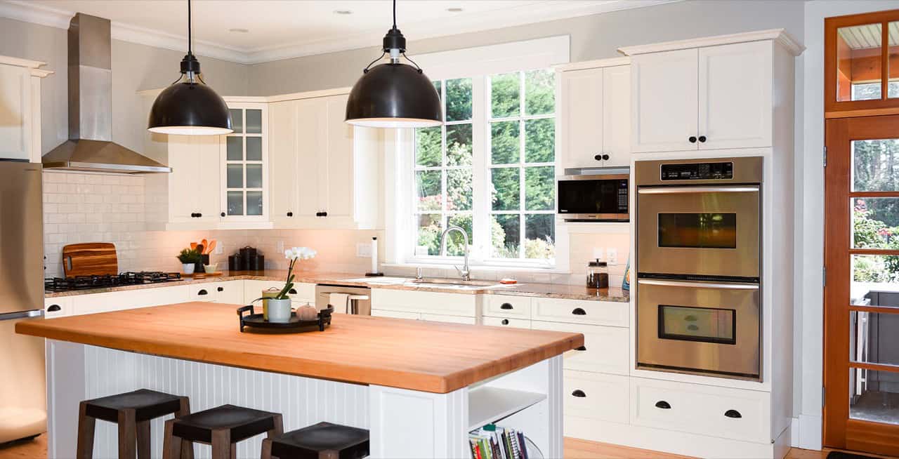Modern white kitchen with island, pendant lights and built-in double ovens in Victoria BC home.