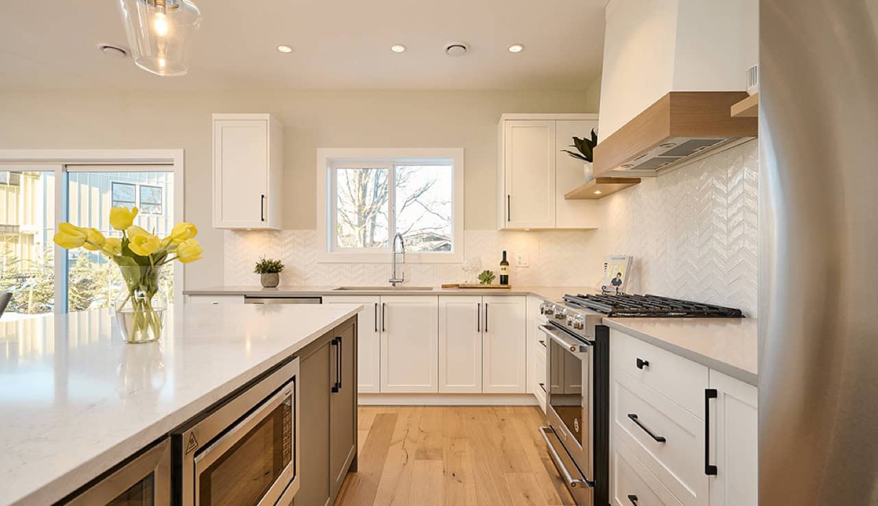 Modern white kitchen with island, stainless steel appliances, and bright natural light.