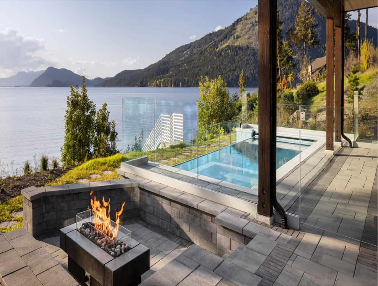 Lakeside outdoor living area with fire pit, pool, and mountain views in Victoria BC.