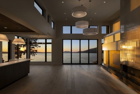 Modern interior with large windows overlooking water and sunset, open-plan living space by WhiteWolf.