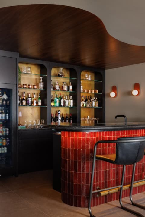 Contemporary home bar with red tiled curved counter and dark wood shelves.