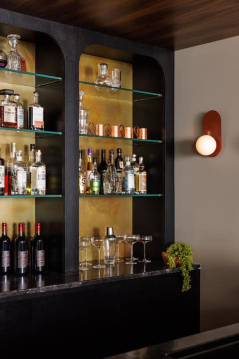 Modern home bar with liquor bottles on illuminated shelves in a dark cabinet.