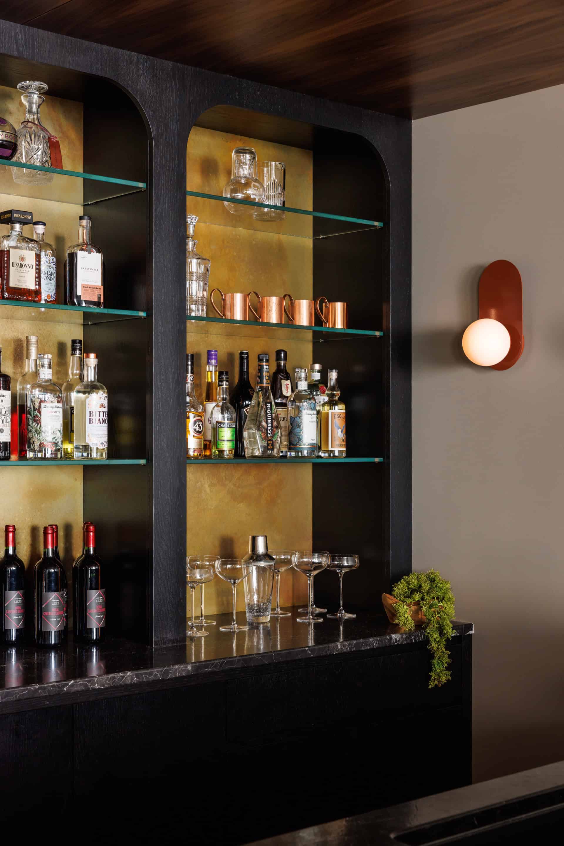 Modern home bar with liquor bottles on illuminated shelves in a dark cabinet.