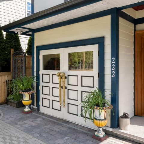 Modern white garage door with decorative panels and brass handles at a blue-trimmed home, numbered.