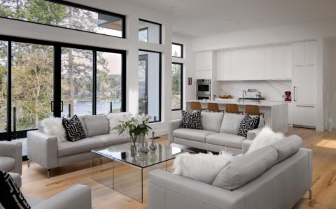 Bright living room with white sofas, large glass windows and modern open kitchen.