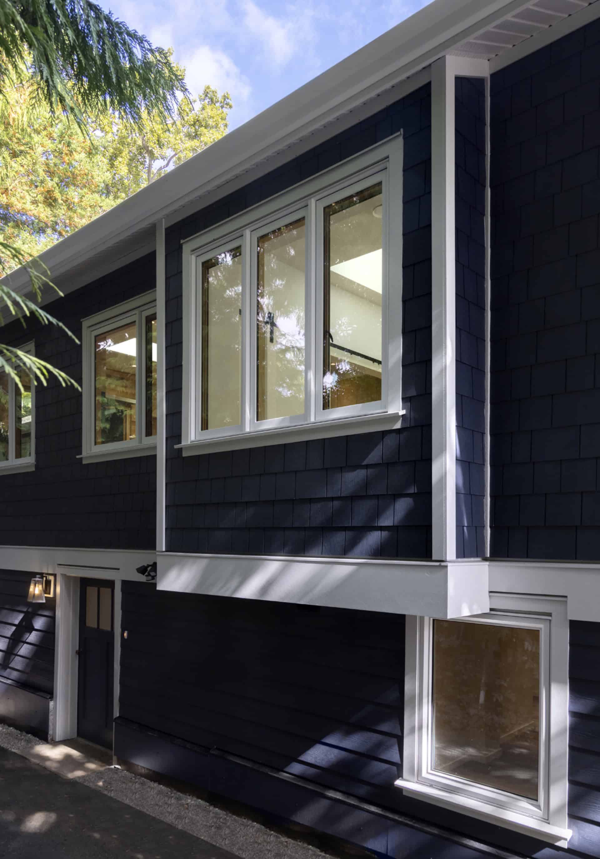 Blue modern home exterior with white-framed windows and shadowed landscaping.