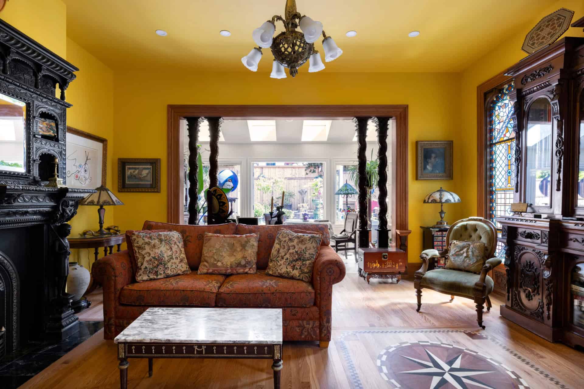 Victorian-style living room with yellow walls, ornate dark wood furniture, and a sunlit conservatory.