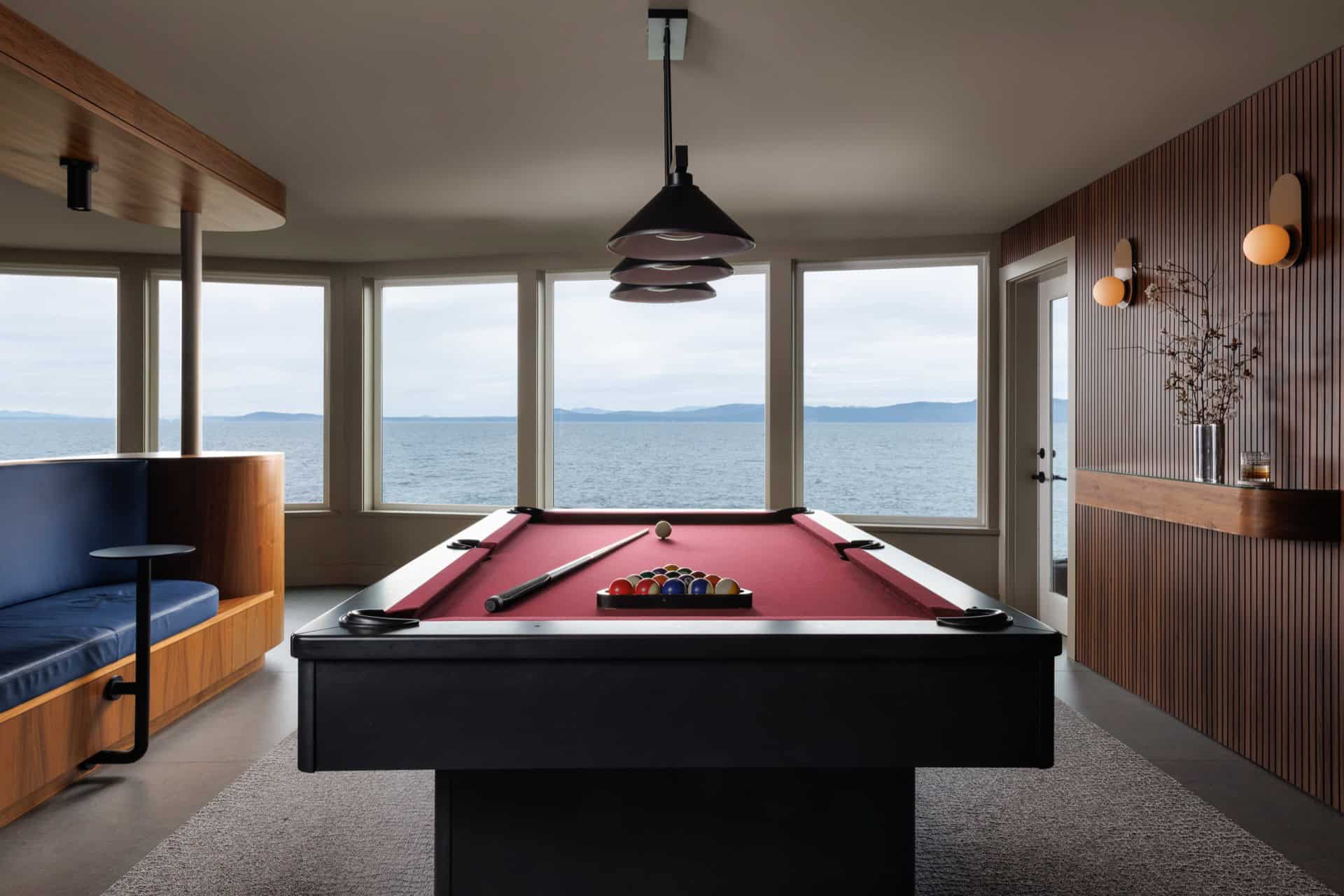 Modern game room with red pool table and ocean view through large windows.