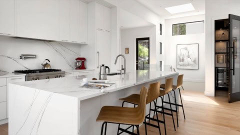 Modern white kitchen with marble countertops and wooden bar stools by Baylight.