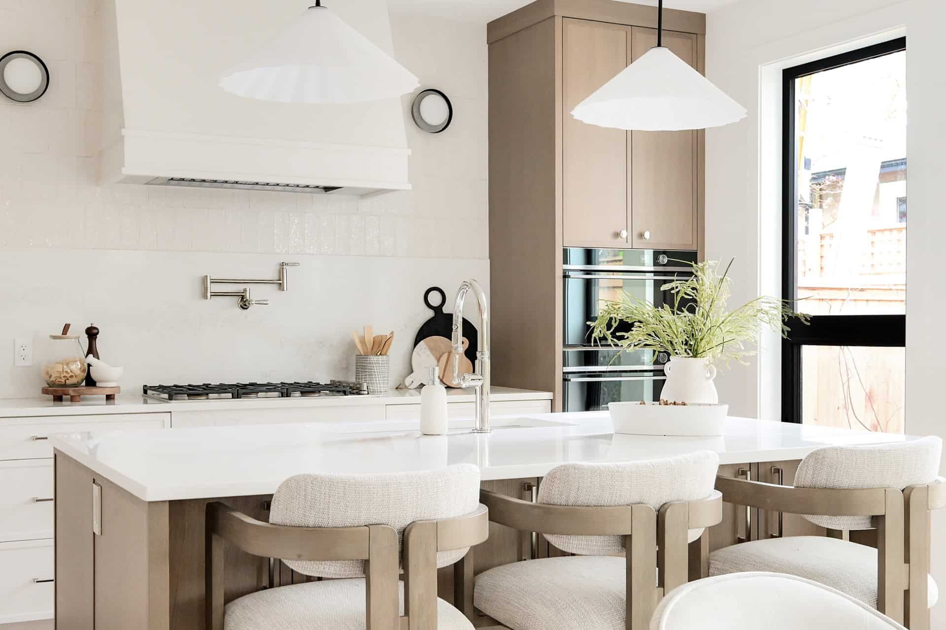 Modern white kitchen with island, pendant lights, and bar seating in Victoria BC home by White Wolf.