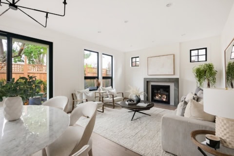 Bright living room with large windows, modern neutral furniture, and a fireplace in a white-toned, V.
