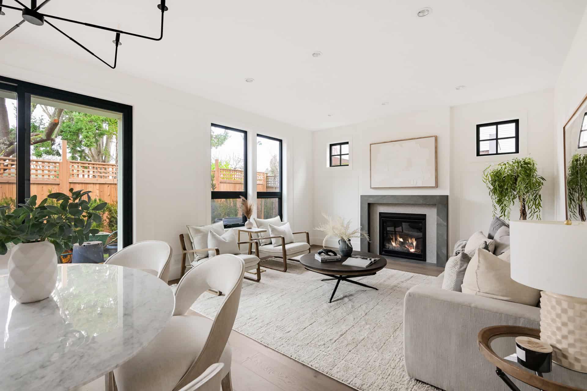 Bright living room with large windows, modern neutral furniture, and a fireplace in a white-toned, V.