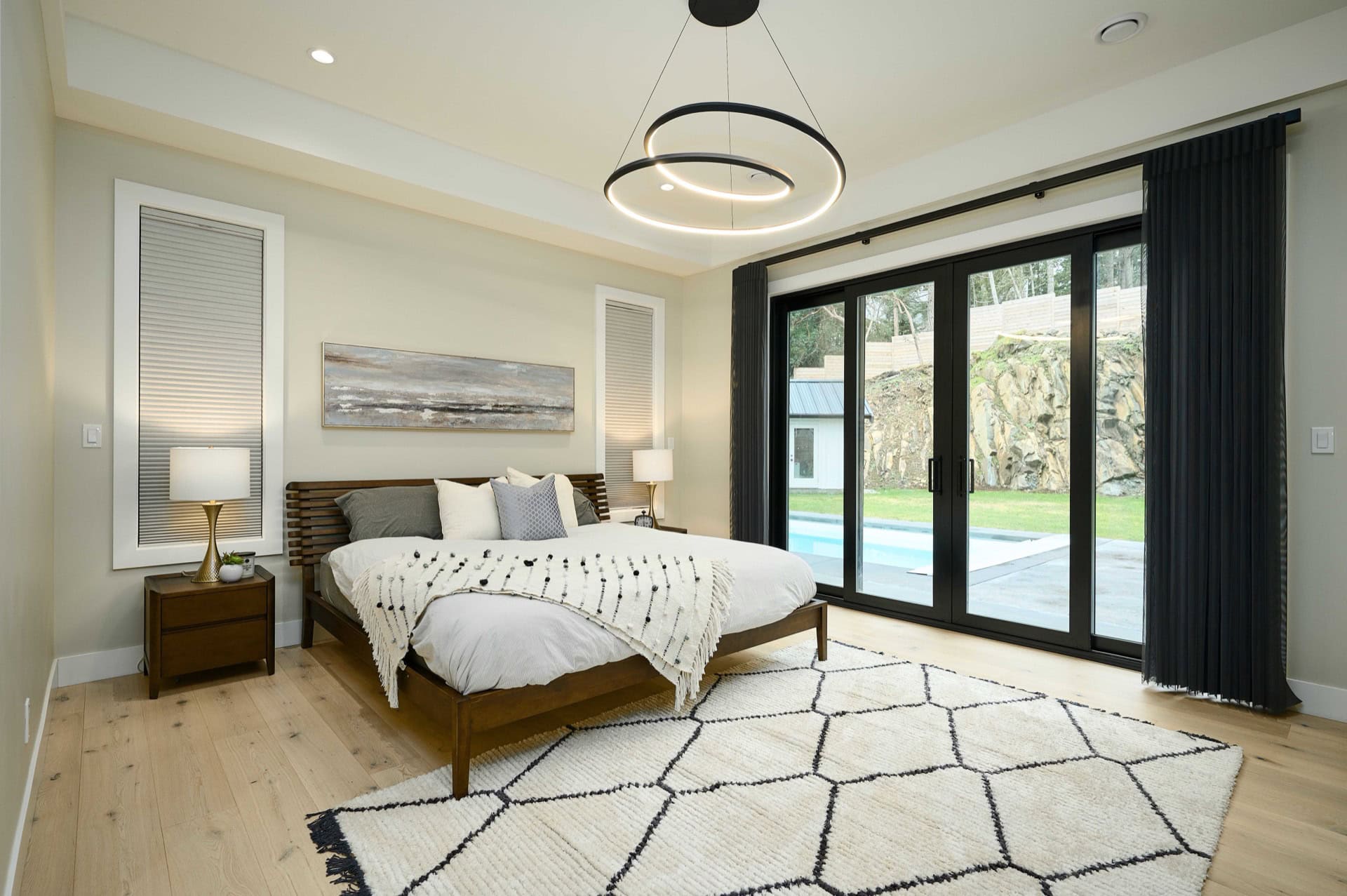 Modern master bedroom with large glass doors opening to a garden and a geometric rug.