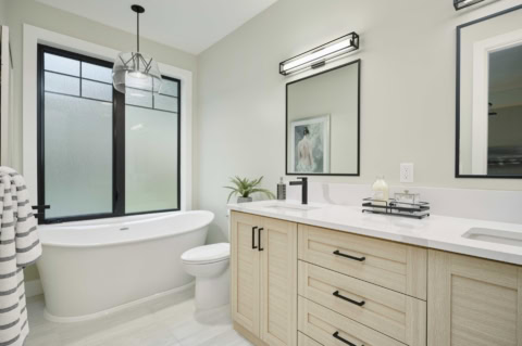 Modern bathroom with freestanding tub and double vanity in light wood cabinetry.