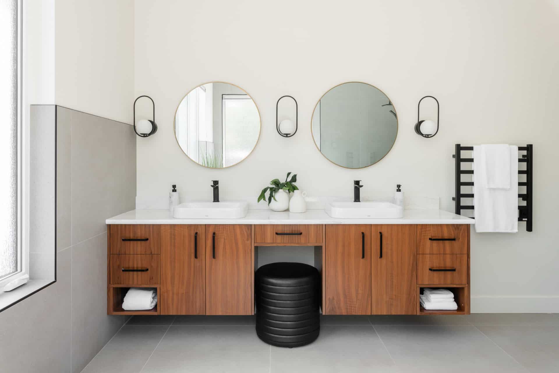 Modern bathroom with dual sinks, wooden vanity, circular mirrors and black wall sconces.