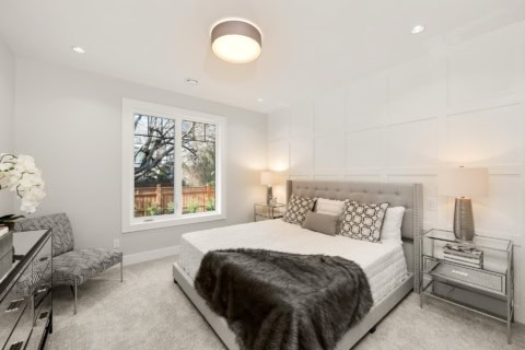 Bright modern bedroom with white panel wall, grey bed, and soft lighting.