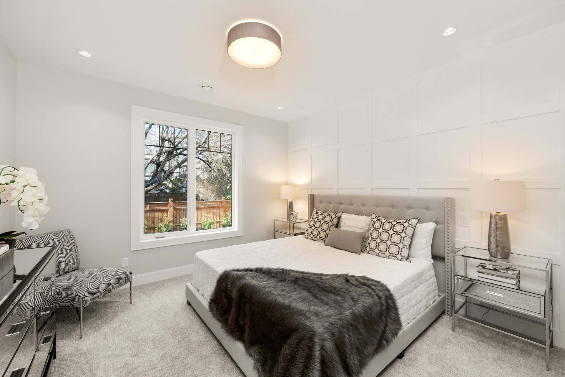 Bright modern bedroom with white panel wall, grey bed, and soft lighting.