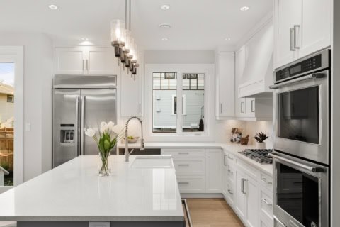 Bright white kitchen with island, stainless steel appliances, and modern pendant lights.