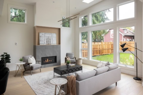 Bright living room with a modern fireplace, large windows, and neutral seating.