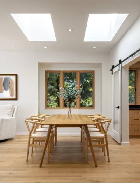 Clean, bright dining area with wooden table and chairs under skylights in a modern home.