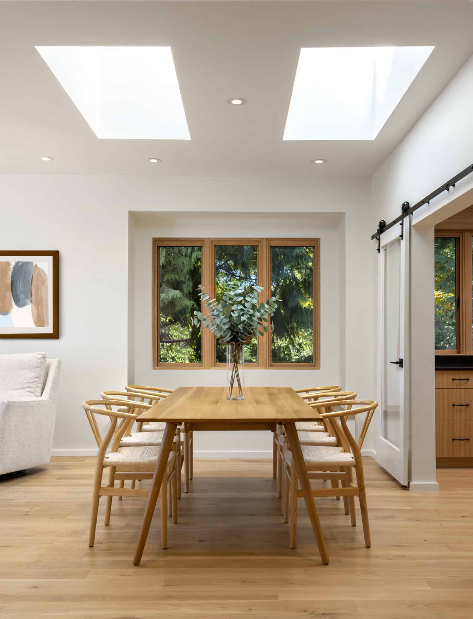 Clean, bright dining area with wooden table and chairs under skylights in a modern home.