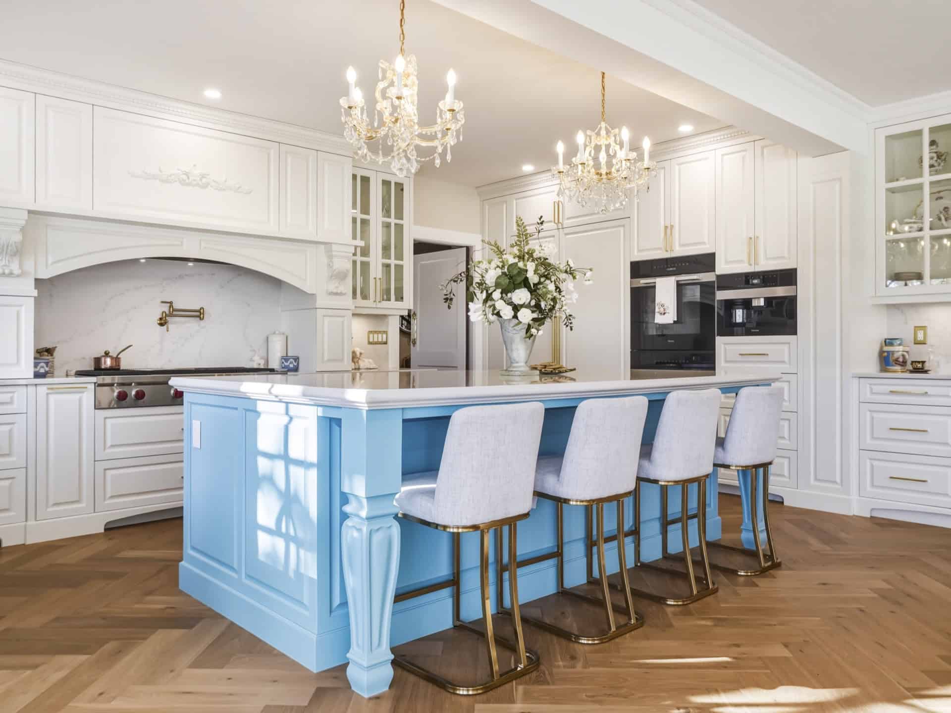 Bright kitchen with white cabinetry and a blue island featuring gold legs and four upholstered barst.