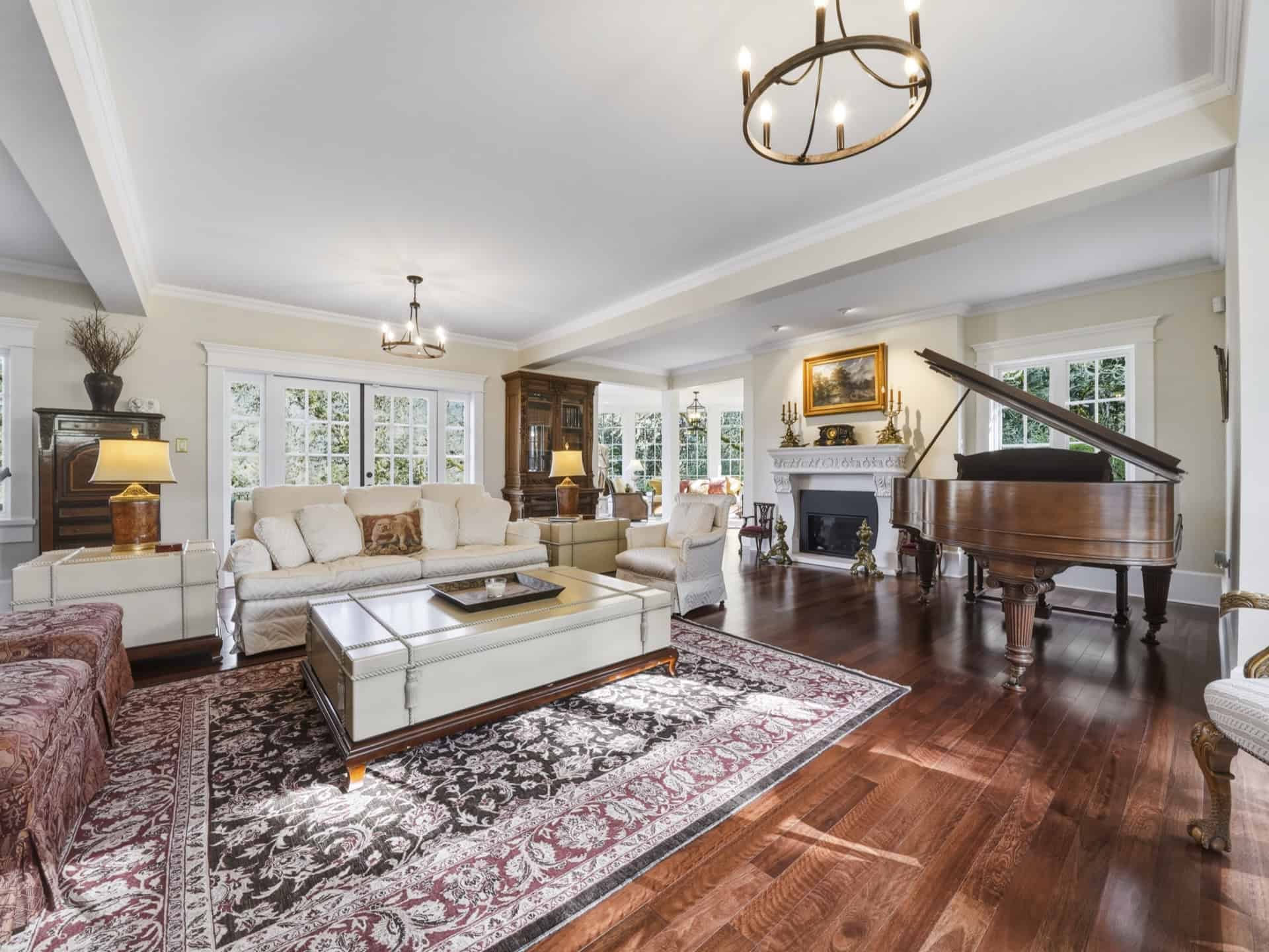 Spacious living room with fireplace, grand piano, hardwood floors and neutral furnishings.