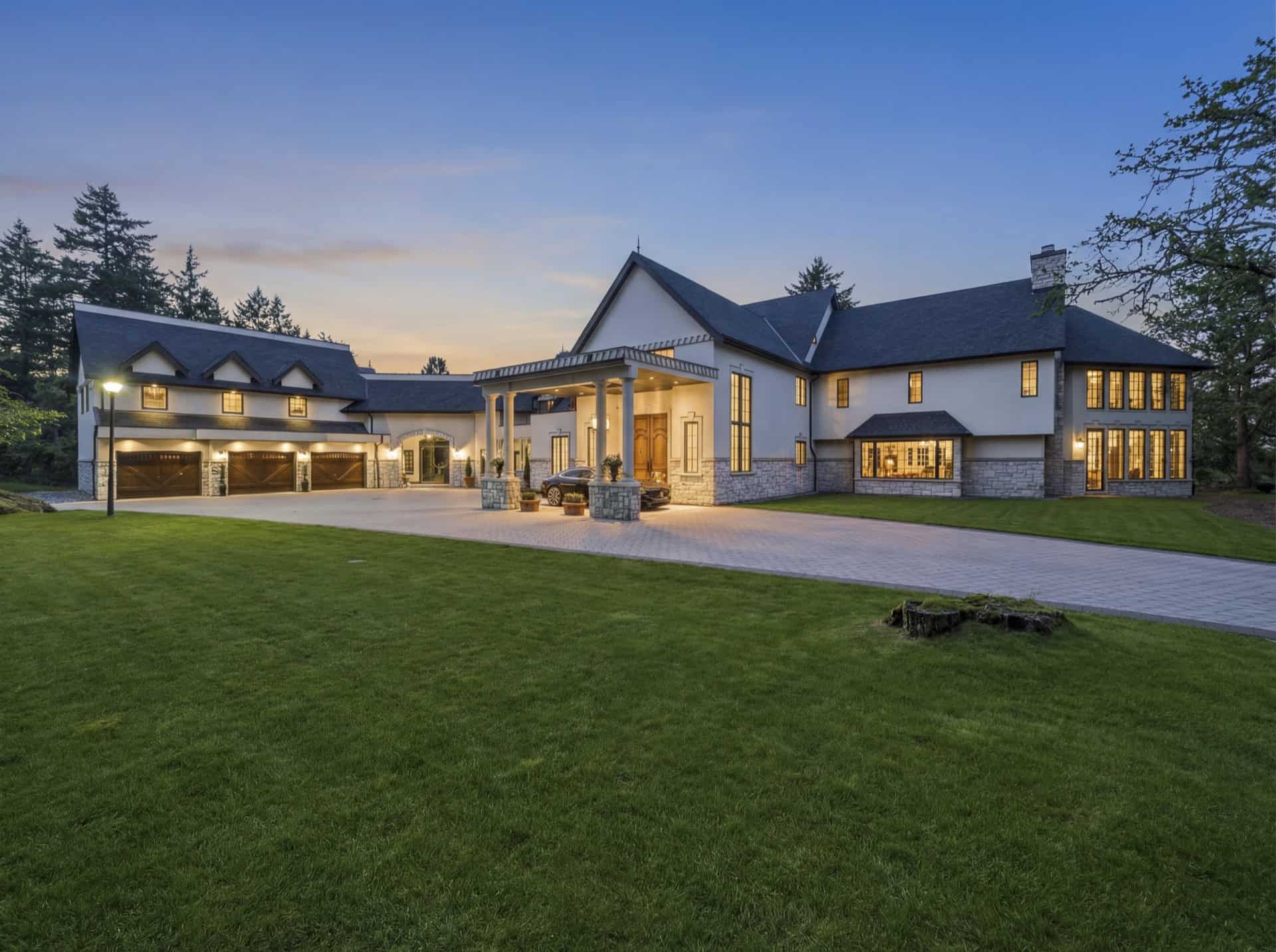 Victoria BC custom home exterior at sunset with stone accents and illuminated entrance.