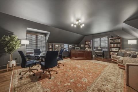 Interior of a luxury home office with dark walls, wooden desk, seating, bookshelves and warm area.
