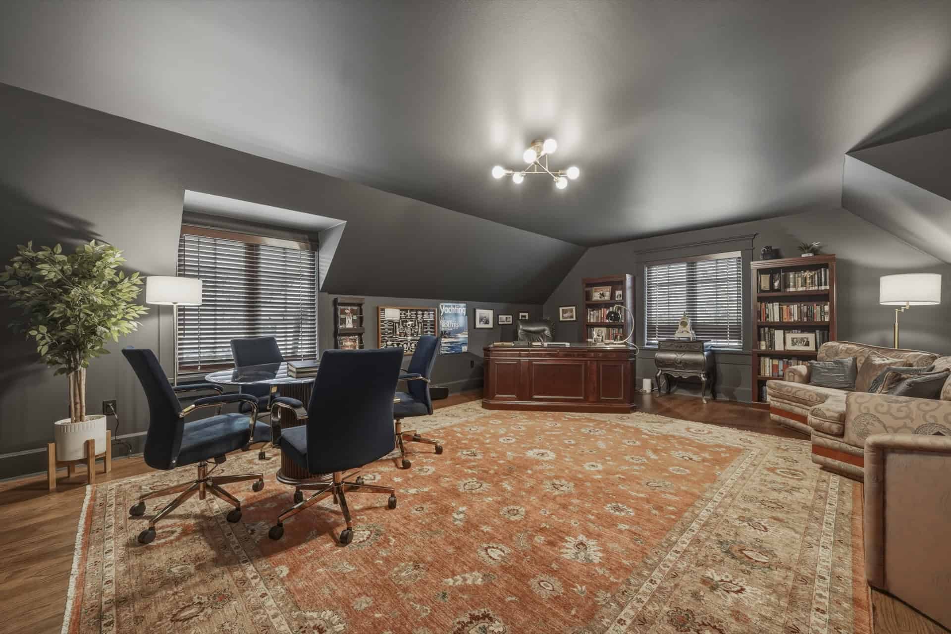 Interior of a luxury home office with dark walls, wooden desk, seating, bookshelves and warm area.