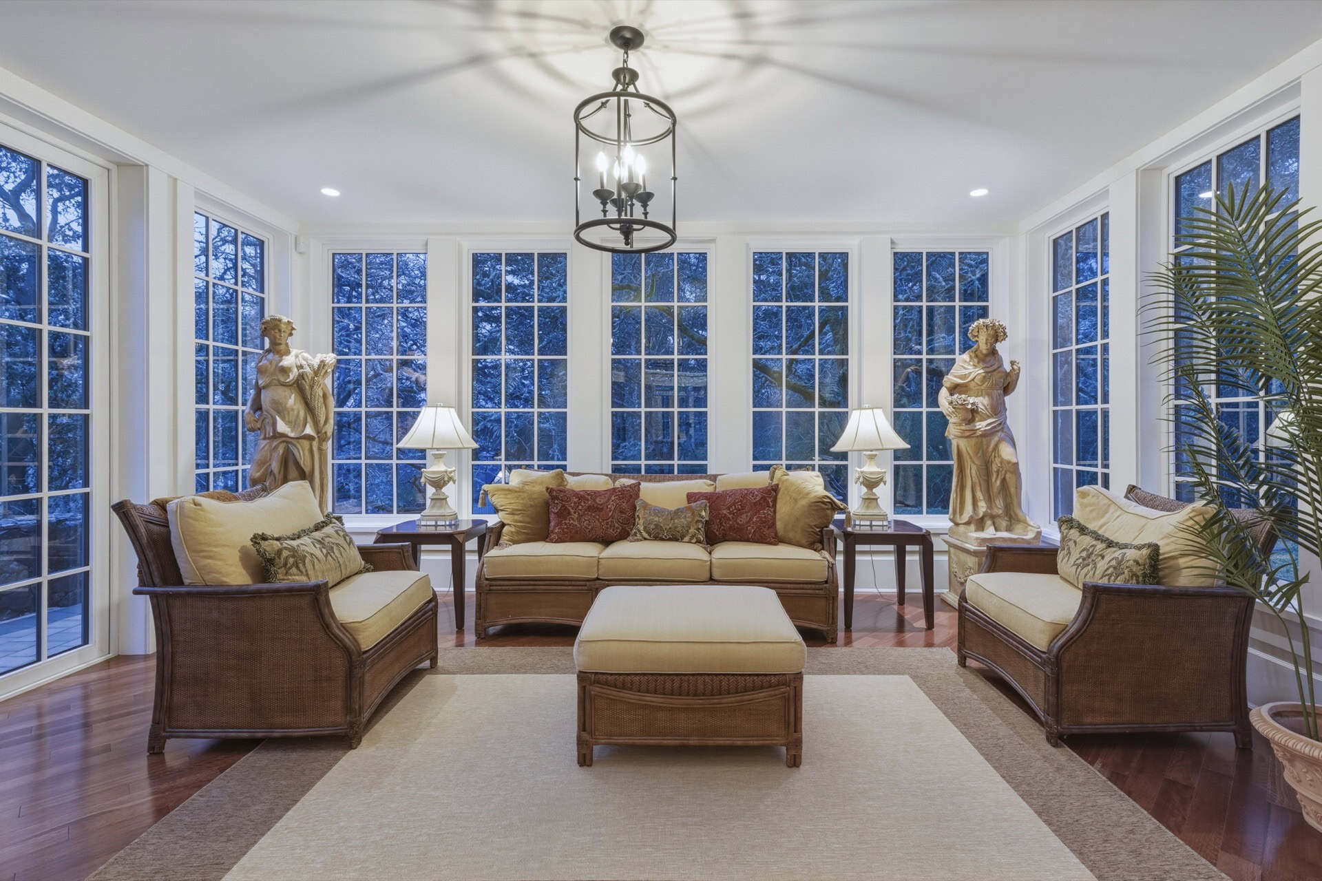 Bright sunroom with wicker sofas, cream cushions, statues, and large windows at The Parkwood Estate.