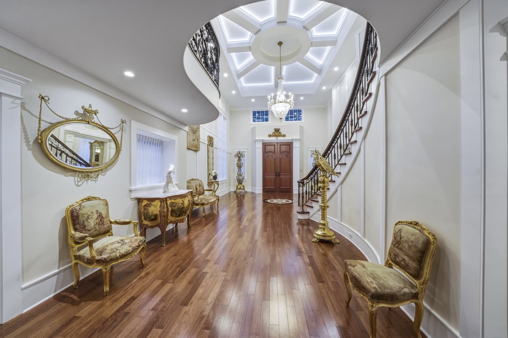 Elegant Victorian-inspired foyer with curved staircase, ornate chairs, and chandelier in Parkwood, a.