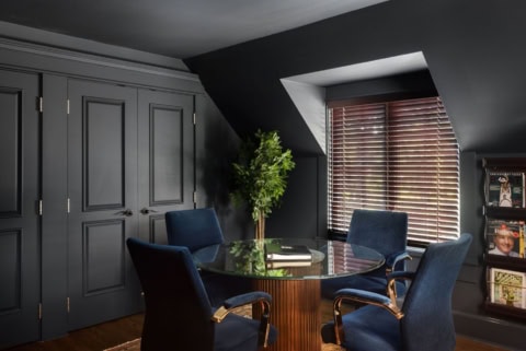 Dark modern meeting room with round glass table and blue chairs under a sloped ceiling.